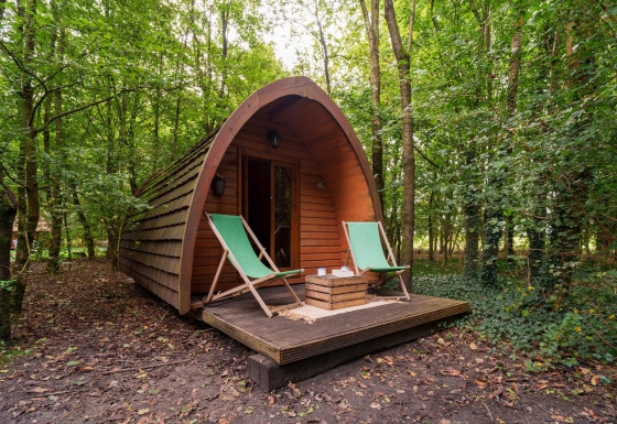 Gran cápsula de madera Duo Pod Large con terraza y dos tumbonas verdes en el bosque de RØSTIG Dorst, Países Bajos.