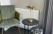 Stijlvol salonhoekje met groene stoel, rond zwart tafeltje en motiefpouf bij North Sea DeLuxe, Vakantiepark de Zeeuwse Parel.