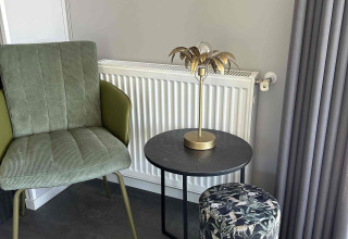 Stijlvol salonhoekje met groene stoel, rond zwart tafeltje en motiefpouf bij North Sea DeLuxe, Vakantiepark de Zeeuwse Parel.