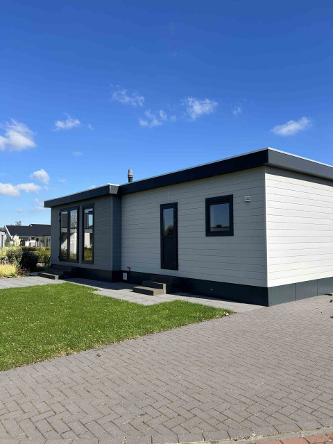 Moderne North Sea DeLuxe lodge met plat dak, grote ramen en een grasveld onder een blauwe hemel.