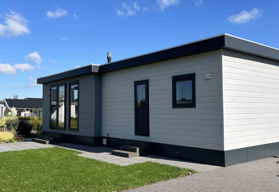 Moderna cabaña North Sea DeLuxe con techo plano, grandes ventanales y césped bajo un cielo azul despejado.