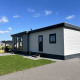 Moderne lodge ved navn North Sea DeLuxe med fladt tag, store vinduer og velplejet have under blå himmel.