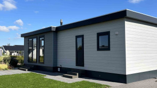 Moderne North Sea DeLuxe lodge met plat dak, grote ramen en een grasveld onder een blauwe hemel.