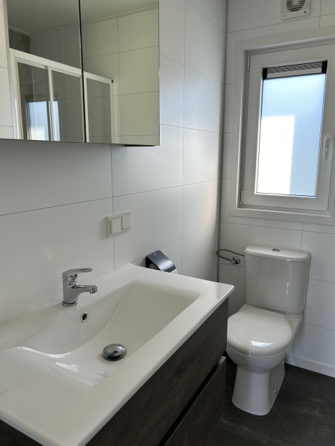 Baño moderno con lavabo blanco, inodoro, armario con espejo y ventana en North Sea DeLuxe, Vakantiepark de Zeeuwse Parel.