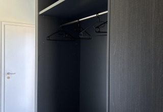 Zwarte kast met legplanken en kleerhangers in North Sea DeLuxe, Vakantiepark de Zeeuwse Parel, Nederland.