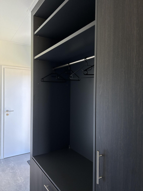 Black wardrobe with shelves and hangers inside North Sea DeLuxe at Vakantiepark de Zeeuwse Parel, Netherlands.