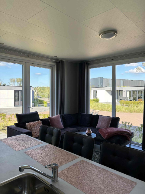 Modern living room at North Sea DeLuxe lodge in Vakantiepark de Zeeuwse Parel, Netherlands, with large windows.