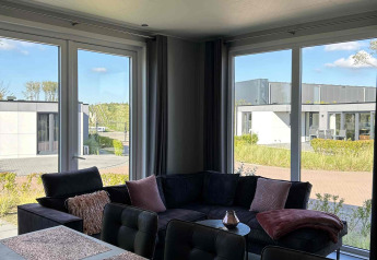 Modern living room at North Sea DeLuxe lodge in Vakantiepark de Zeeuwse Parel, Netherlands, with large windows.