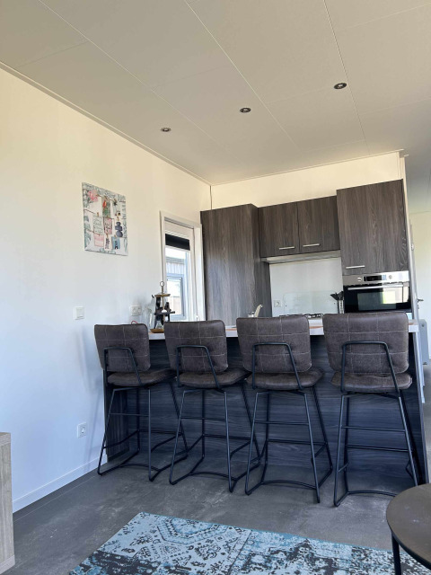 Modern kitchen and bar area with four high chairs in a North Sea DeLuxe lodge at Vakantiepark de Zeeuwse Parel.