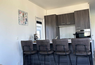Moderne keuken met bar en vier hoge stoelen in een North Sea DeLuxe lodge in Vakantiepark de Zeeuwse Parel.