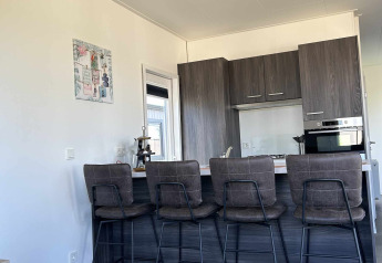 Moderne køkken og barområde med fire høje stole i en lodge på North Sea DeLuxe, Vakantiepark de Zeeuwse Parel.