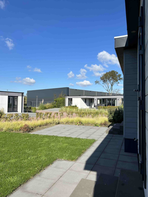 Zicht op moderne lodges en tuin onder blauwe lucht aan North Sea DeLuxe, Vakantiepark de Zeeuwse Parel.