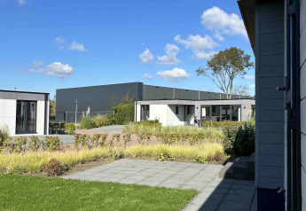 Blick auf moderne Lodge und Garten bei sonnigem Wetter im North Sea DeLuxe, Vakantiepark de Zeeuwse Parel.