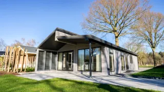 Lodge moderne Hackfort Hottub 6 avec grandes baies vitrées, terrasse, arbres et pelouse sous le soleil.