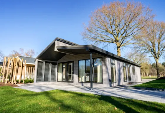Moderne lodge genaamd Hackfort Hottub 6 met grote ramen, terras en groene omgeving op een zonnige dag.