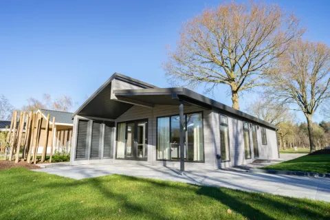 Moderne Lodge Hackfort Hottub 6 mit großen Fenstern, Terrasse und Bäumen bei sonnigem Wetter.