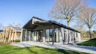 Moderne Lodge Hackfort Hottub 6 mit großen Fenstern, Terrasse und Bäumen bei sonnigem Wetter.