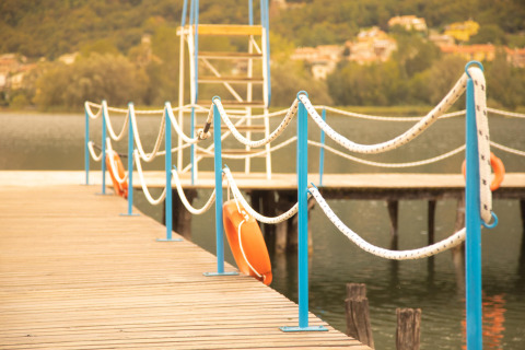 Pontile in legno con corrimano blu e salvagenti al Camping Al Lago di Lago, Veneto, Italia.