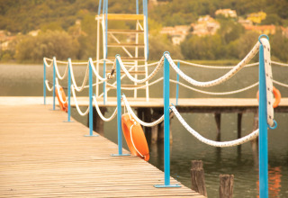 Muelle de madera con barandillas azules y aros salvavidas en Camping Al Lago di Lago, Véneto, Italia.