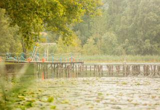 Muelle con trampolín y aros salvavidas en un lago tranquilo rodeado de árboles en Veneto, Italia.