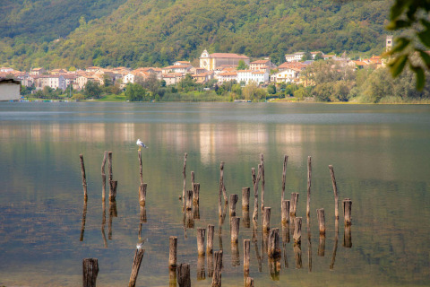 Vista del lago en Camping Al Lago di Lago, Véneto, Italia, con postes de madera y el pueblo al fondo.