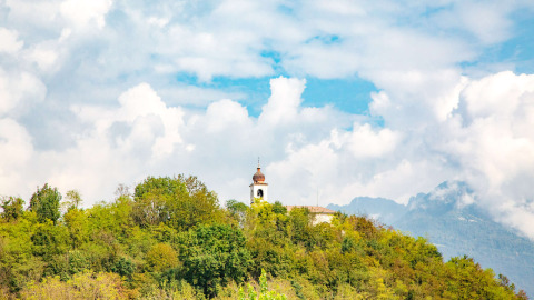 Kerktoren tussen bomen bij Camping Al Lago di Lago in Veneto, Italië, onder een bewolkte blauwe hemel.