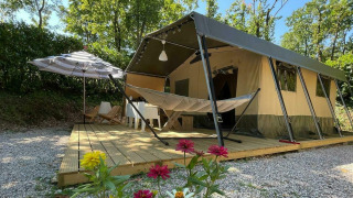 Safari tent Base Lodge with wooden deck, hammock, parasol, flowers in foreground, and green trees behind.