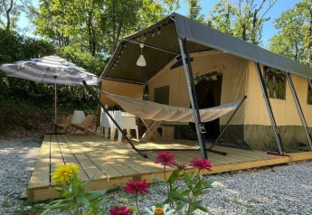 Safari tent Base Lodge with wooden deck, hammock, parasol, flowers in foreground, and green trees behind.