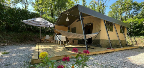 Safari-Zelt Base Lodge mit Holzterrasse, Hängematte, Sonnenschirm, Blumen und grünem Wald dahinter.