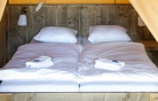 Cama en la tienda safari Base Lodge en Camping Al Lago di Lago, Italia, con sábanas blancas y pared de madera.