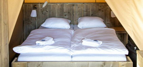 Cama en la tienda safari Base Lodge en Camping Al Lago di Lago, Italia, con sábanas blancas y pared de madera.