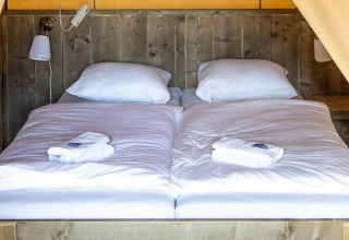 Cama en la tienda safari Base Lodge en Camping Al Lago di Lago, Italia, con sábanas blancas y pared de madera.