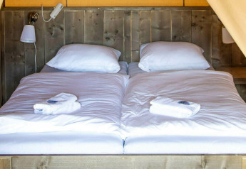 Cama en la tienda safari Base Lodge en Camping Al Lago di Lago, Italia, con sábanas blancas y pared de madera.