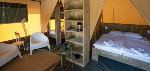 Interior de una tienda safari en Base Lodge con cama doble, litera, área de estar y mobiliario moderno.