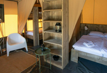 Interior de una tienda safari en Base Lodge con cama doble, litera, área de estar y mobiliario moderno.