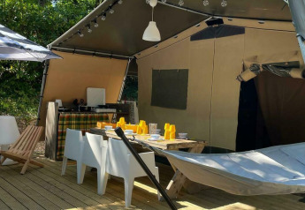 Tienda safari Base Lodge en Camping Al Lago di Lago en Italia, con terraza, tumbonas, hamaca y comedor al aire libre.