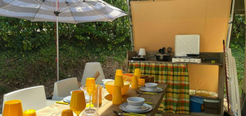 Area pranzo all’aperto con tavolo, sedie e cucina sotto un ombrellone alla Base Lodge, Camping Al Lago di Lago, Italia.