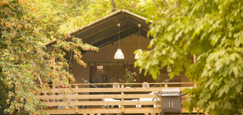 Safari-Zelt Wood Lodge auf Camping Al Lago di Lago in Italien, umgeben von grüner Natur und Bäumen.