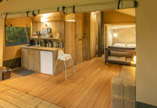 Vista interior de una tienda safari en Wood Lodge, Camping Al Lago di Lago, Italia, con cocina y área de estar.