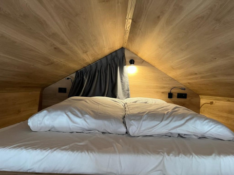 Cama cómoda con sábanas blancas en una diminuta casa de madera en Tiny House at Hoge Kempen, Bélgica.