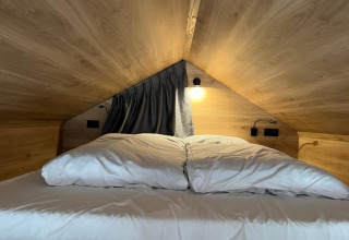 Seng med hvide lagner i et lille træhus på Tiny House at Hoge Kempen, Belgien, set i loftsrummet.