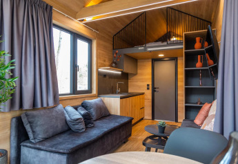 Moderne, kompakt stue og køkken i Tiny House ved Hoge Kempen i Belgien, indrettet med træ og gråt møblement.