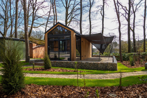 Modern tiny house in the woods at Hoge Kempen, Belgium, with wooden exterior and shaded outdoor terrace.