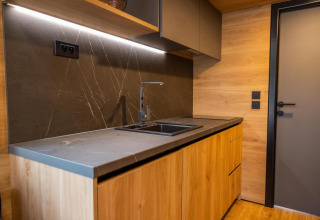 Modern tiny house kitchen with wood cabinets, black countertop, and sink in Hoge Kempen, Belgium.