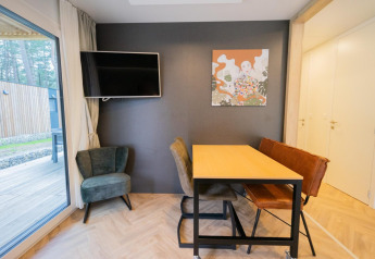 Moderne stue i Thor cottage, Hoge Kempen, Belgien, med vindue, vægkunst, TV og spisestuehjørne.