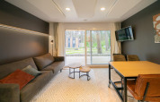 Sala luminosa en la cabaña Thor, Hoge Kempen, Bélgica, con sofá, TV, mesa y vista al bosque exterior.