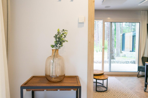Stylish interior at Thor Cottage, Hoge Kempen, Belgium, featuring a glass vase on a wooden table by window.