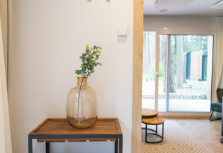 Stylish interior at Thor Cottage, Hoge Kempen, Belgium, featuring a glass vase on a wooden table by window.