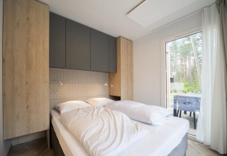Dormitorio moderno en la cabaña Thor en Hoge Kempen, Bélgica, con cama cómoda y gran ventana con vistas al bosque.