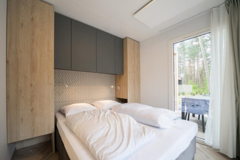 Dormitorio moderno en la cabaña Thor en Hoge Kempen, Bélgica, con cama cómoda y gran ventana con vistas al bosque.